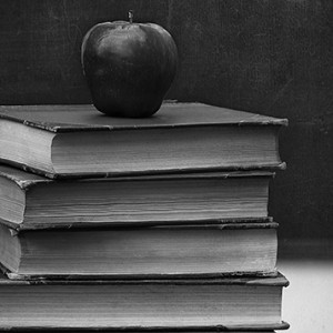 Pile of old books on desk with blackboard in background
